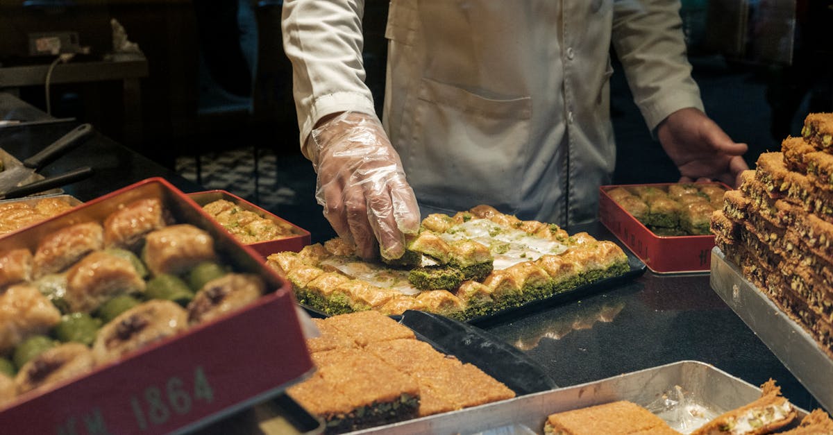 From above of anonymous crop male in gloves and white robe putting delicious fresh sweet dessert in container in local bakery shop